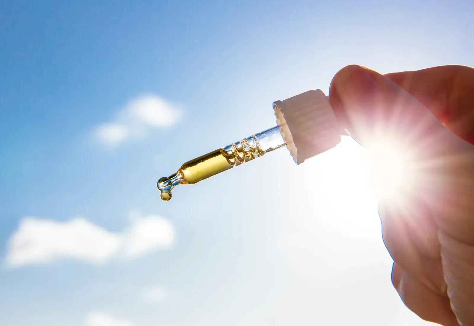 Une main tient une pipette de vitamine D en gouttes devant le soleil